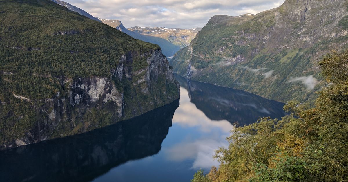 A serene, reflective view of a Norwegian fjord surrounded by lush green mountains.