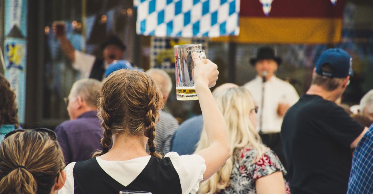 A lively crowd at an outdoor Oktoberfest celebration with beer mugs raised in the air.