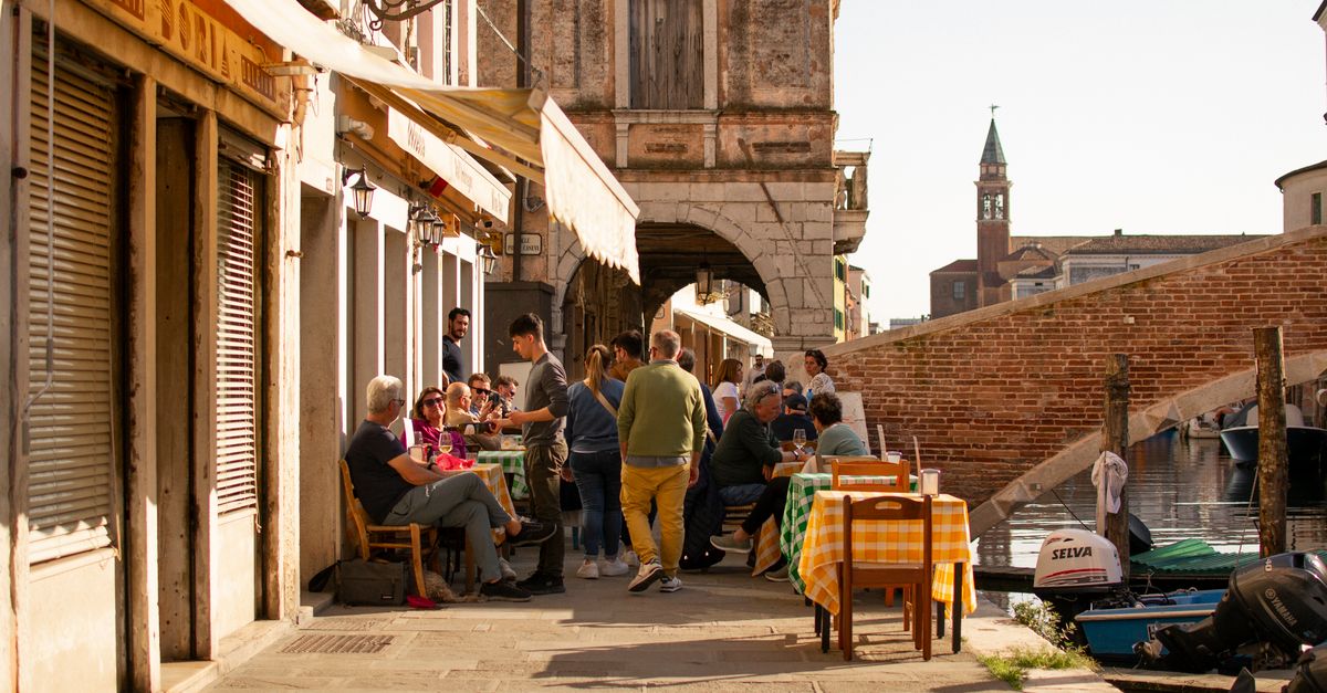 A sunny outdoor café scene in Chioggia, Italy, with people dining at tables.
